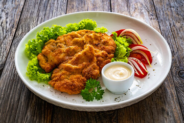 Crispy breaded seared chicken cutlet with lettuce and tomatoes on wooden table
