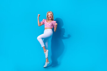 Full body photo of pretty young girl raise fists celebrate lucky dressed stylish pink cherry print outfit isolated on blue color background