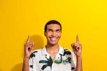 Portrait of positive guy wear print clothes with ring in nose look directing up at offer empty space isolated on yellow color background