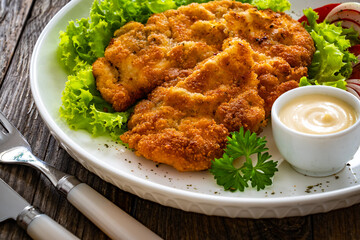 Crispy breaded seared chicken cutlet with lettuce and tomatoes on wooden table
