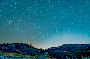 Route de montagne avec un ciel étoilé et vue de M45 et de Neptune