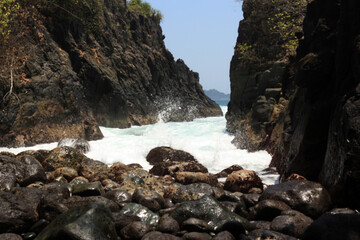 Obraz premium Waves splashing against rocks and pebblesin the seashore. Bright sunny day in the rocky beach.