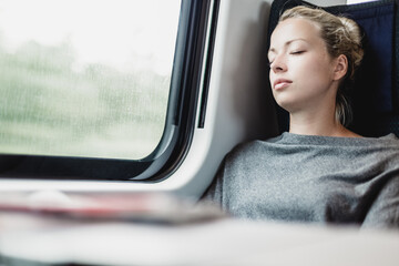 Blonde casual caucasian lady napping while traveling by train.