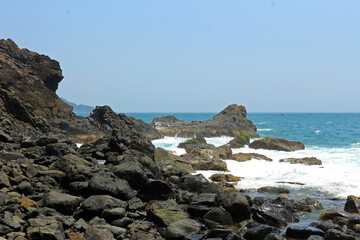 Fototapeta na wymiar Waves splashing against rocks in the seashore. Bright sunny day in the rocky beach.