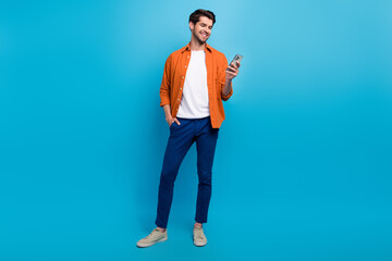 Full body photo of cheerful young man hold use smart phone chatting blogging isolated on blue color...
