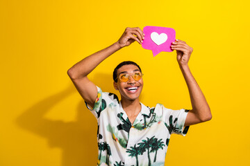 Photo of positive attractive guy wear trendy outfit hands above head showing instagram facebook like isolated on yellow color background - obrazy, fototapety, plakaty