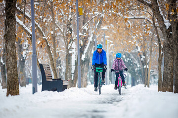Father and child ride bicycles in winter. A man and his daughter ride bicycles along a bike path in...