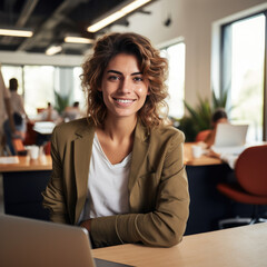 Casual shot of a smiling businesswoman behind her laptop at her working desk looking at the camera, daylight