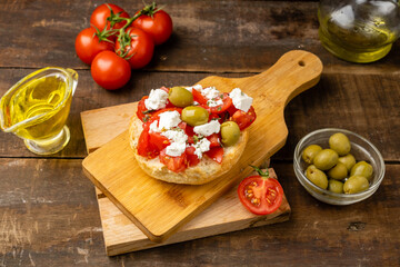 Greek cuisine, dakos with fresh tomatoes and olives, wooden table.