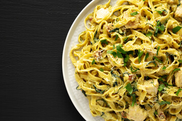 Homemade Creamy Chicken Bacon Pesto Pasta on a Plate on a black background, top view. Flat lay, overhead, from above. Space for text.