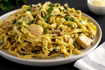 Homemade Creamy Chicken Bacon Pesto Pasta on a Plate on a black background, side view.