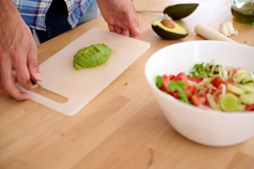 A chopped ripe organic avocado fruit on a cutting board on the wooden table with a bowl of fresh healthy vegan salad