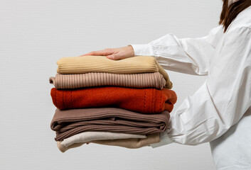 Woman hands holding stack warm winter sweaters on grey background. A stack of sweaters, jumpers in...