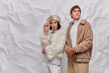 asian woman in eyeglasses, faux fur jacket and mittens near stylish man on white textured backdrop