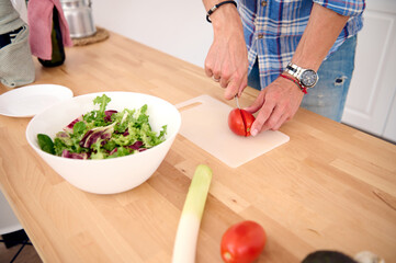 Close-up of a male chef cutting fresh ripe organic juicy tomatoes while preparing a healthy diet salad in the kitchen.