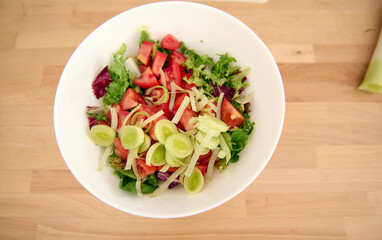 Top view white bowl with fresh healthy salad from organic vegetables and greens on a wooden table. Alimentation. Dieting