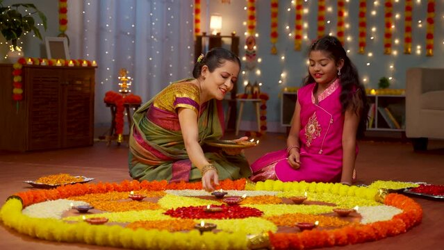 Happy Grandmother with girl grandchild placing diya lamps on Flower rangoli - concept of diwali festival preparation, Tradition ritual or custom and Generations