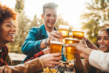 Group of multi ethnic friends having backyard dinner party together - Diverse young people sitting at bar table toasting beer glasses in brewery pub garden - Happy hour, lunch break and youth concept - obrazy, fototapety, plakaty