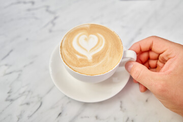  Cup of hot cappuccino. The table in the coworking space of the coffee shop. A cup of coffee on the veranda on a sunny day. Coffee break at the cafe. Close-up