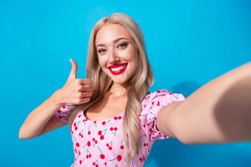 Photo portrait of attractive young woman selfie show thumb up dressed stylish pink cherry print clothes isolated on blue color background