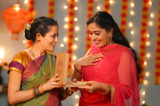 Senior mother giving jewelry necklace gift to daughter at diwali festive celebration at home - concept of special occasion, values and traditional culture