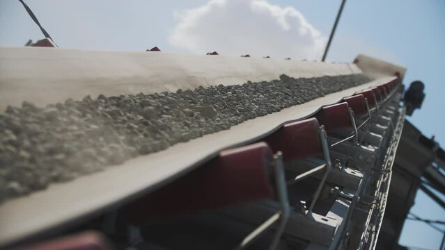 Crushed granite ore transported by conveyor in mining quarry closeup. Automated equipment carries gravel rocks at manufacturing plant