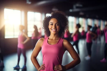 Tuinposter Female personal African-American trainer pink t shirt smiling at camera in gym. Happy woman fitness coach standing in modern club interior. Active sport life getting fit healthy lifestyle concept © Valeriia