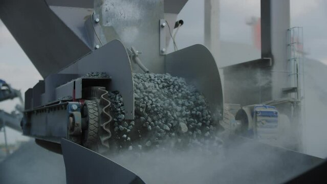 Rotating pulleys loads gravel grains in container at mining quarry. Conveyor carries stone building materials with dust clouds at plant