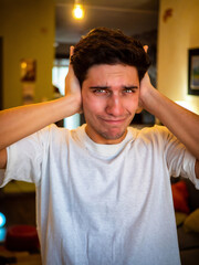 Too much noise: attractive young man covering his ears, indoor at home