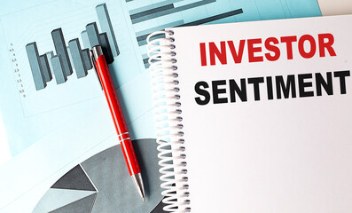 INVESTOR SENTIMENT text on a notebook with pen on a chart background