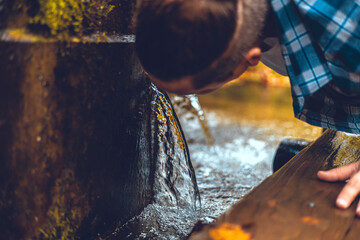 A man bent down to drink clean, cool water from a spring after a walk in the forest. A handsome man...