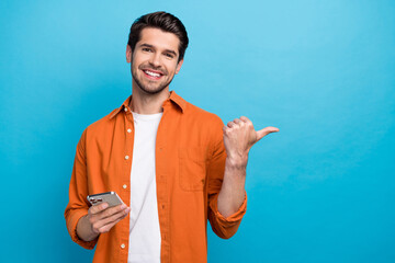 Photo of positive guy beaming smile hold use iphone apple gadget direct finger empty space isolated...
