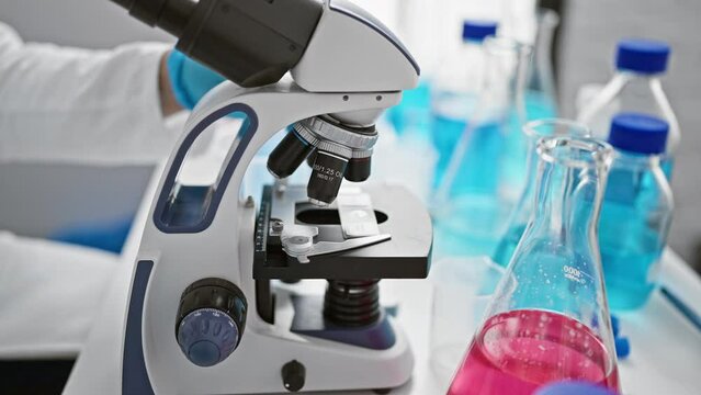 Caucasian male scientist working intensely, eyes fixated on microscope, pouring liquid into test tube sample in lab