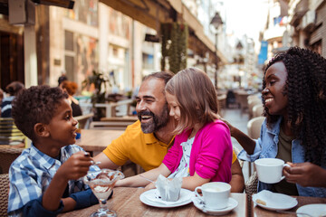 Young blended stepfamily having coffee and desserts together in a outdoor cafe sitting area in the...