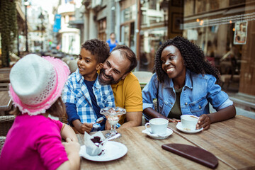 Young blended stepfamily having coffee and desserts together in a outdoor cafe sitting area in the...