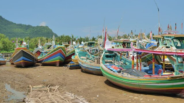Wooden fishing boats are densely parked in a dry harbor on a hot afternoon on the coast of Java, Indonesia. Depicts the decline in fish catches and the number of fishermen who have lost their jobs