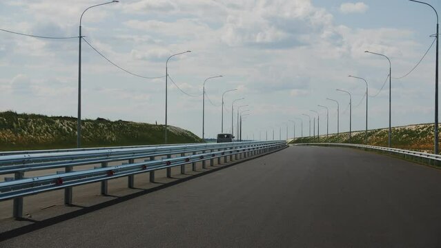 Van drives along highway line separated with barrier fence at countryside. Border of metal on contemporary freeway under cloudy sky