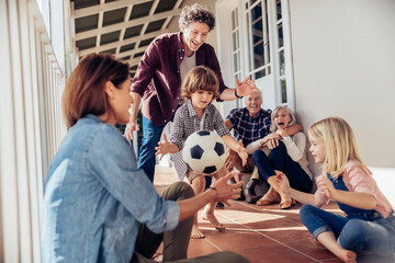 Multigenerational family cheering a young boy kicking a soccer ball on the balcony of their home