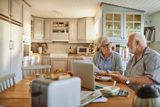 Concerned senior couple going over bills during breakfast in the kitchen