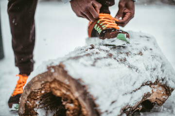 Young man tying his sneakers on a log in a park during winter