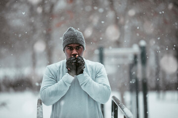 Young fit man warming up his hands before a exercise in a park during snowfall