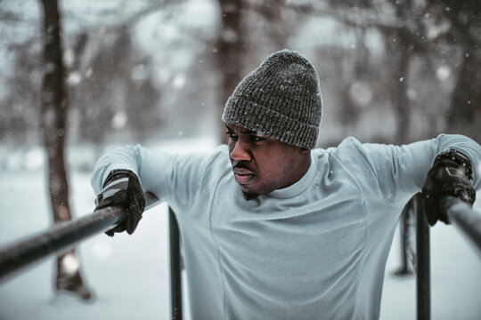 Young fit man doing dips in a outdoor park during snowfall