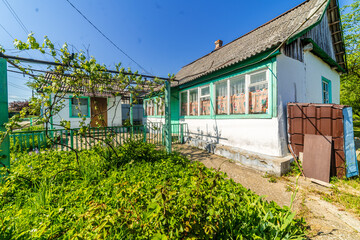 a dilapidated one-story rural house. Green lawn and trees. Whitewashed walls, green window frames.