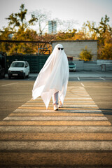 Celebrating halloween. Ghost Challenge 2021. A man dressed as a ghost from a sheet and sunglasses crosses the road along the crosswalk. Spooky season.