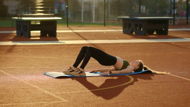 Yong woman doing fitness on a mat on a sports ground.