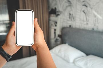 Woman hand holding a modern frameless smartphone with blank white screen on background of a modern bedroom interior