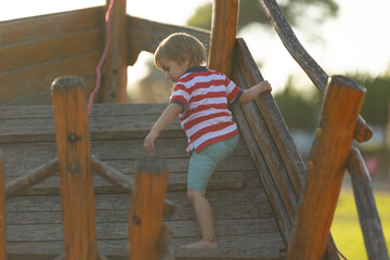 Little cute boy climbing up wooden structure on playground