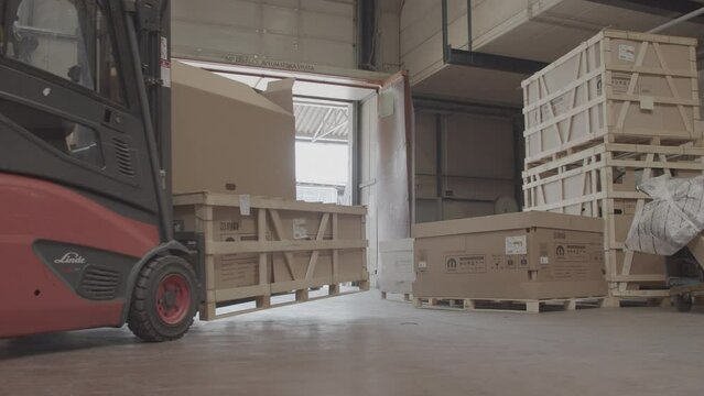 Warehouse worker driving a forklift. Lifting and moving pallets with boxes. Driving out of storage.