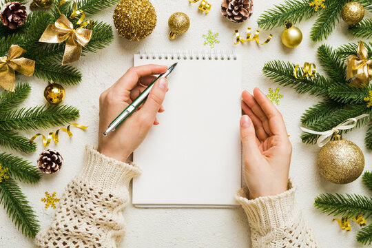 Woman writing Christmas to do list on notebook on colored background with xmas decorations