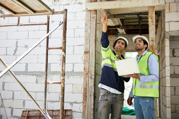 workers or architects working on laptop computer and pointing up to something at construction site